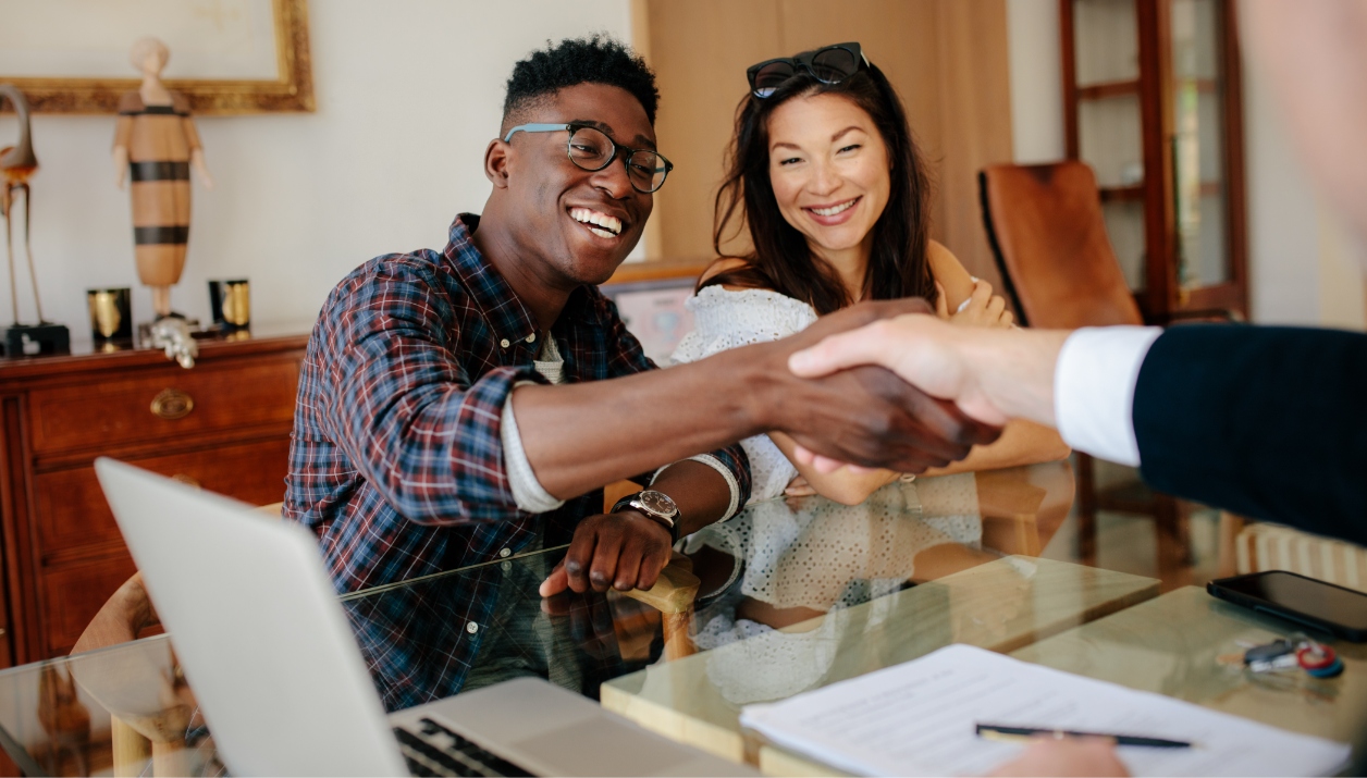 A happy couple shaking hands with an agent.